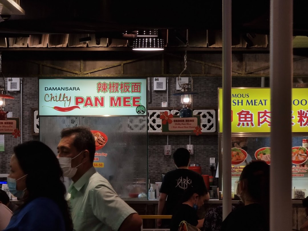An interior shot of a bustling food court with various food stalls, including 'Chilly Pan Mee' and 'Fish Meat Noodle'.