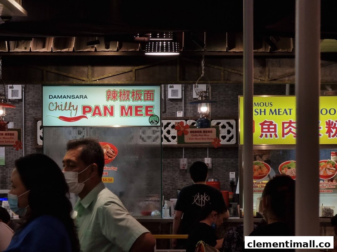 An interior shot of a bustling food court with various food stalls, including 'Chilly Pan Mee' and 'Fish Meat Noodle'.