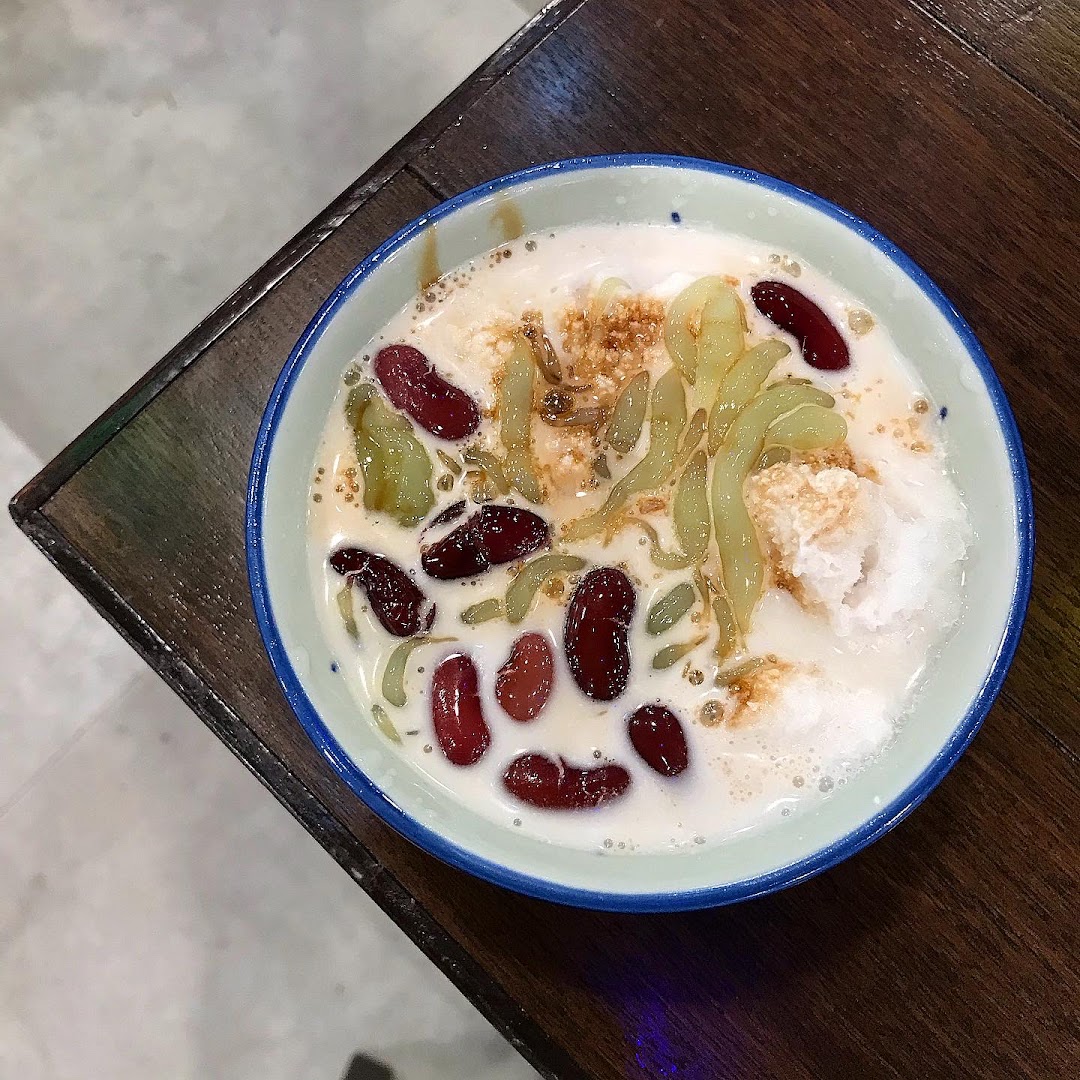 A vibrant bowl of Cendol dessert with red beans, green jelly, and coconut milk on a wooden table.