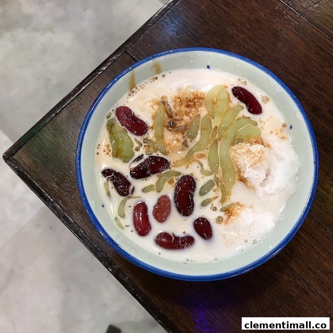 A vibrant bowl of Cendol dessert with red beans, green jelly, and coconut milk on a wooden table.