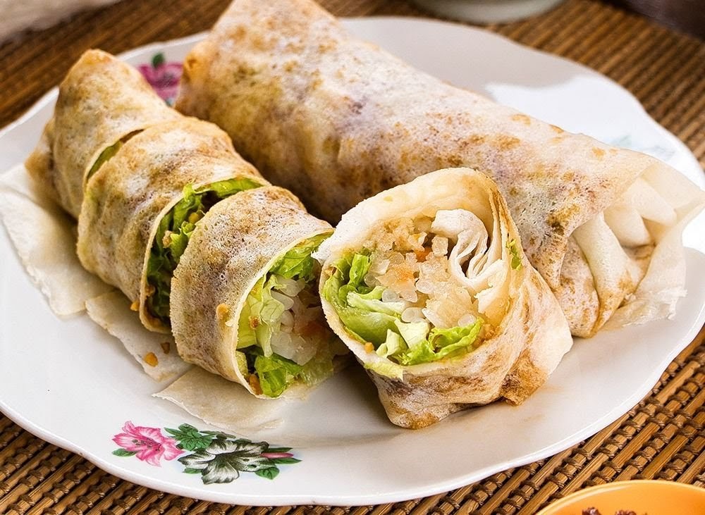 Two fresh spring rolls, one sliced to reveal crisp lettuce and savory filling, served on a white plate.