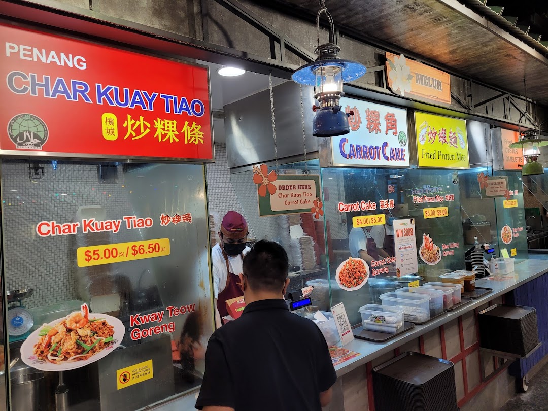 A bustling food stall showcasing various menu items and prices, with staff preparing dishes.