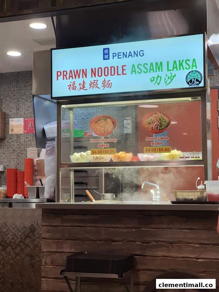 A food stall display board featuring Penang Prawn Noodle and Assam Laksa with prices.