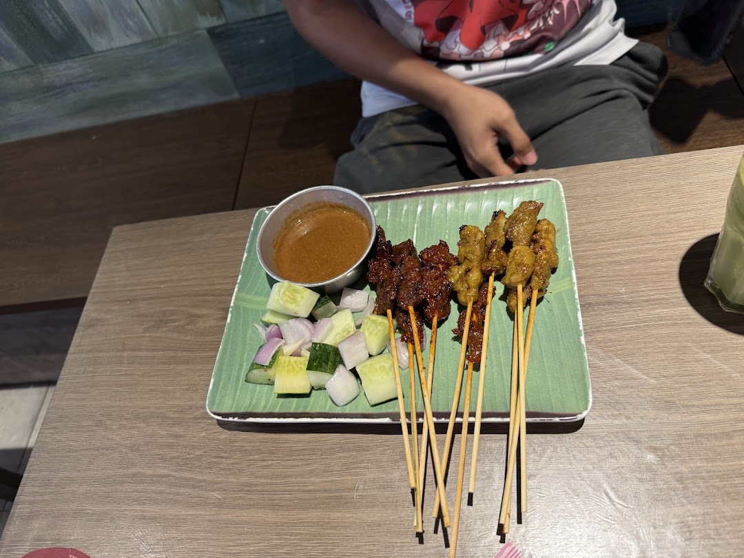 A plate of delicious satay with peanut sauce, cucumber, and onions on a wooden table.