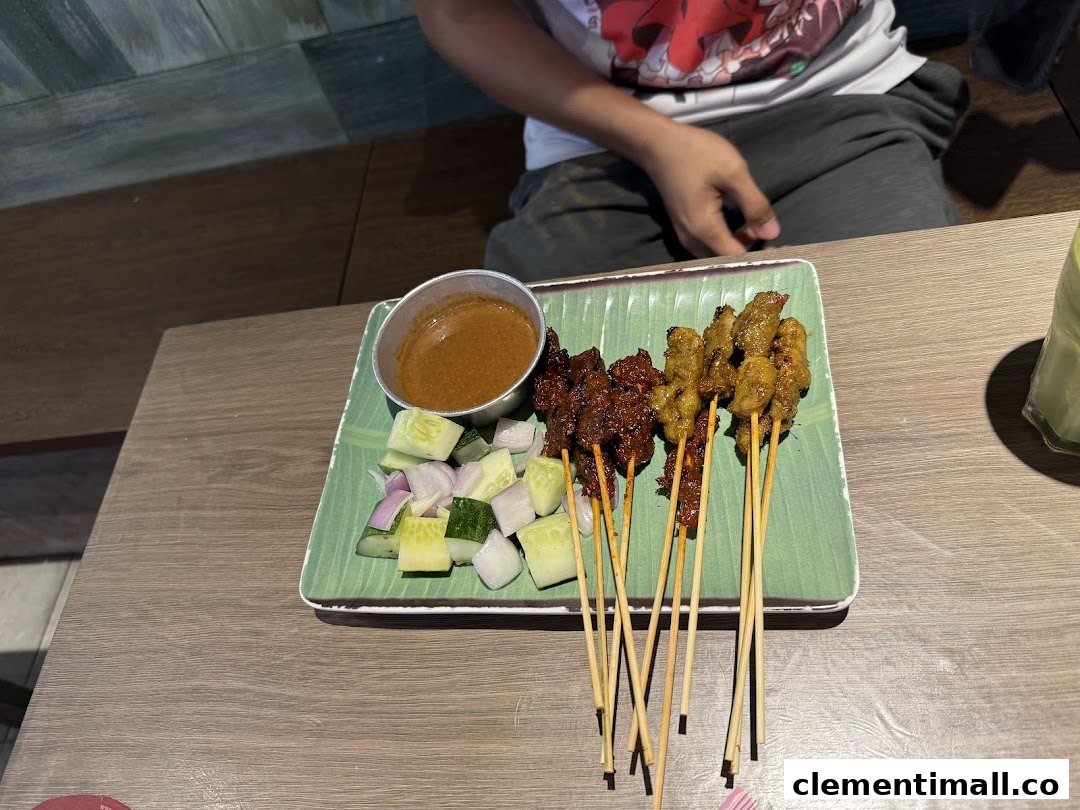 A plate of delicious satay with peanut sauce, cucumber, and onions on a wooden table.