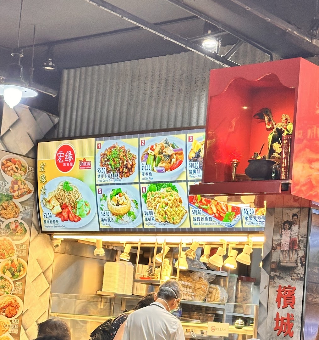 A food stall's menu board displaying various Asian dishes with prices and images, with customers queuing.