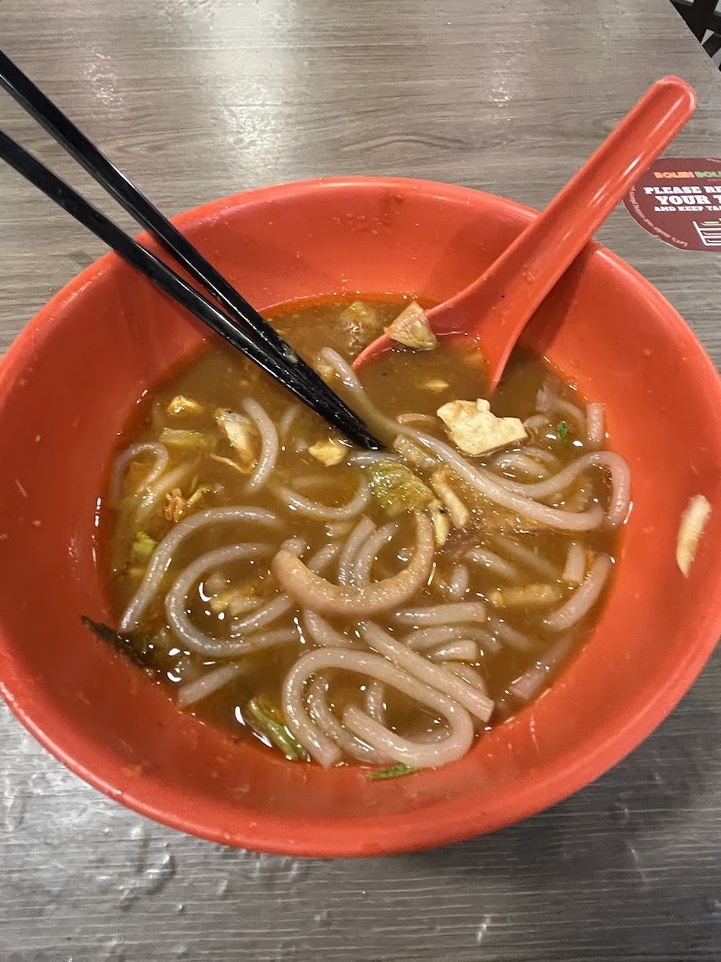 A vibrant orange bowl filled with delicious noodles and broth, served with chopsticks and a spoon.