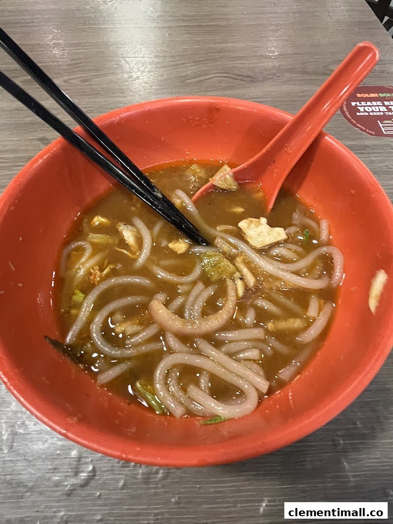 A vibrant orange bowl filled with delicious noodles and broth, served with chopsticks and a spoon.