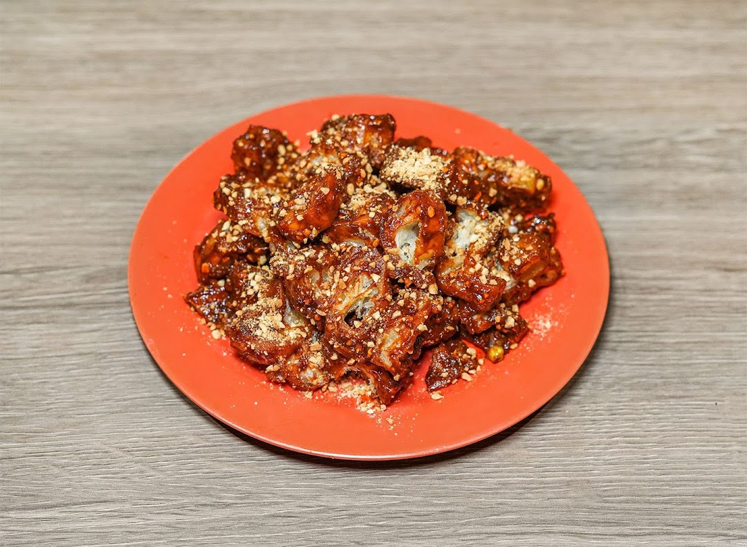 A plate of deep-fried dough fritters coated in sweet sauce and crushed peanuts.
