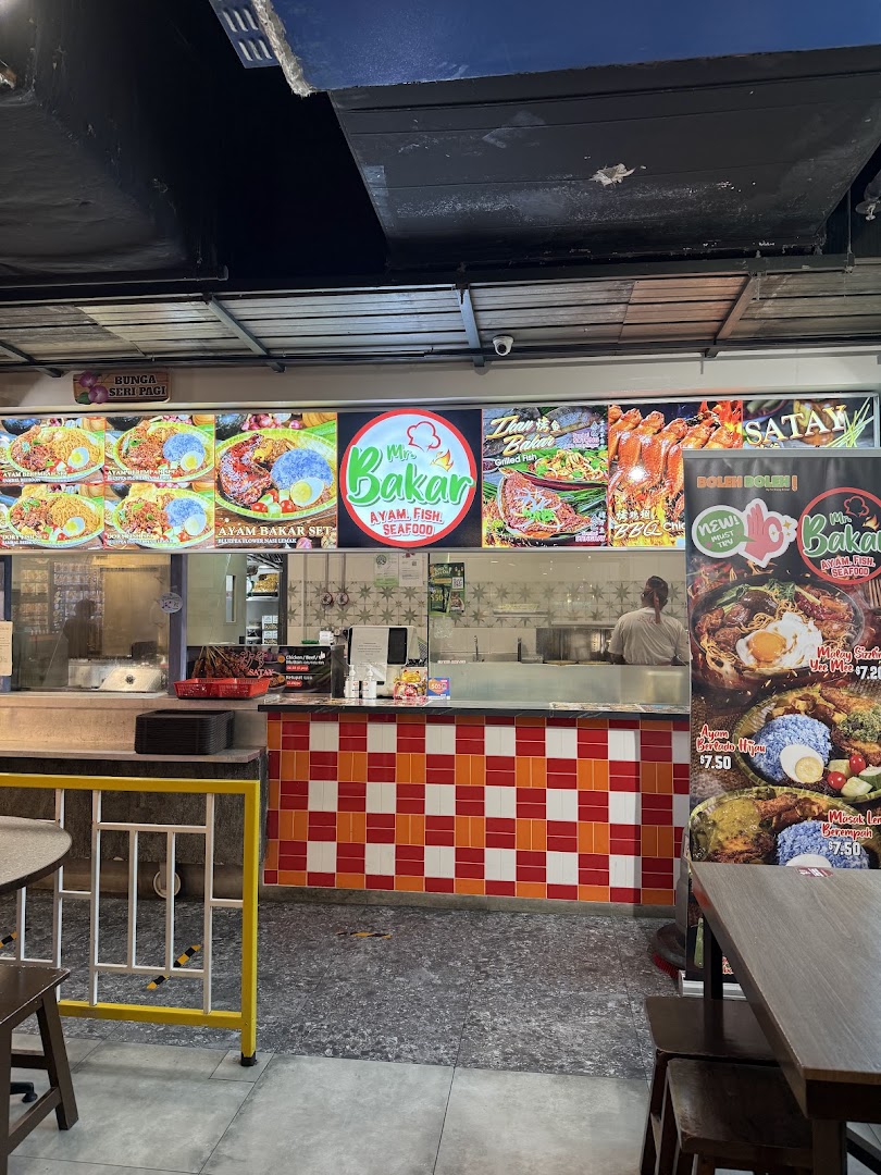 A vibrant food stall counter with illuminated menu displays showcasing various grilled dishes and sets.