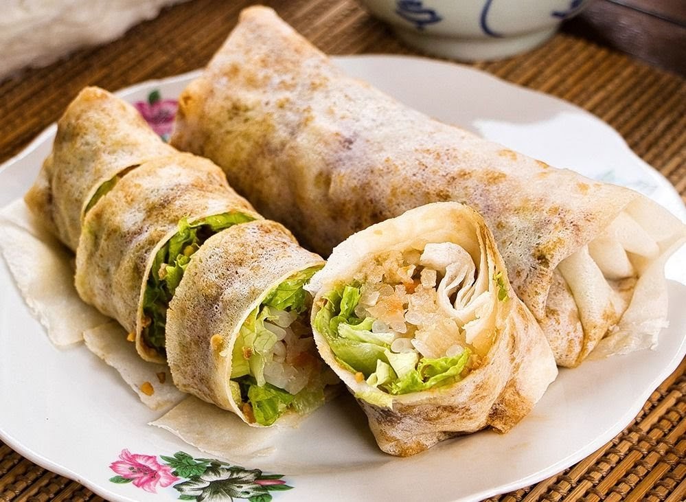 Two fresh popiah (spring rolls) on a plate, one cut to show the crisp lettuce and savory filling.