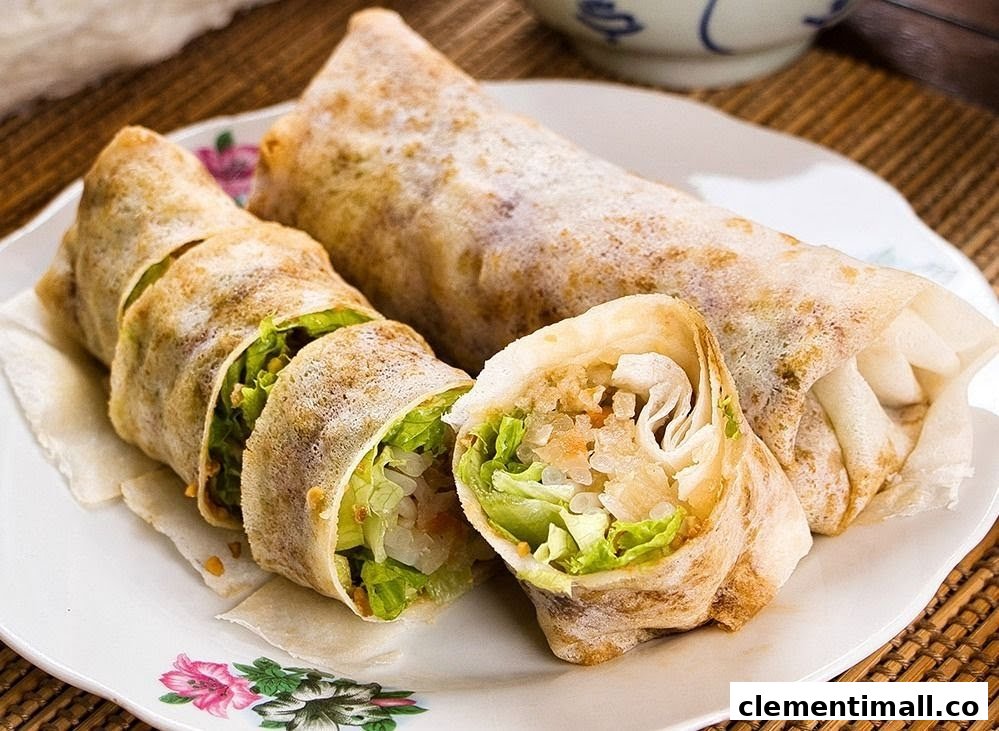 Two fresh popiah (spring rolls) on a plate, one cut to show the crisp lettuce and savory filling.