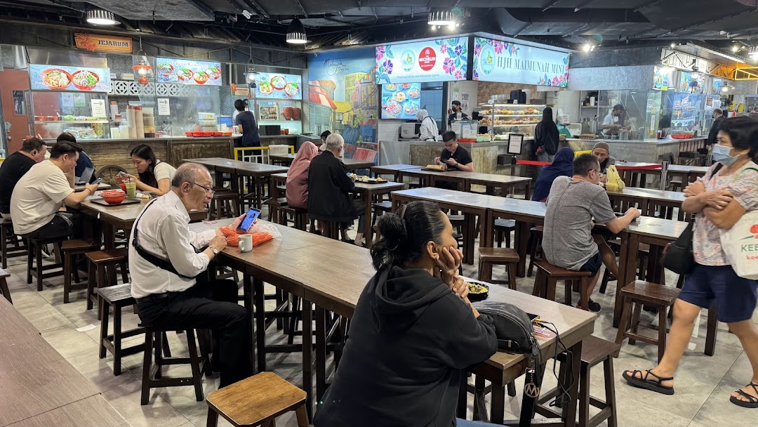 Diners enjoy meals at various food stalls within a bustling food court.