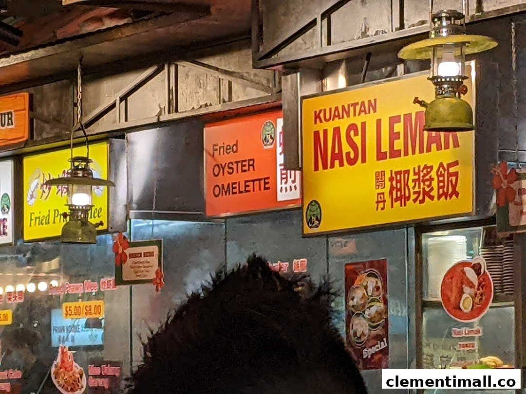 Close-up of a food stall interior featuring signs for Kuantan Nasi Lemak and Fried Oyster Omelette, with vintage lanterns.