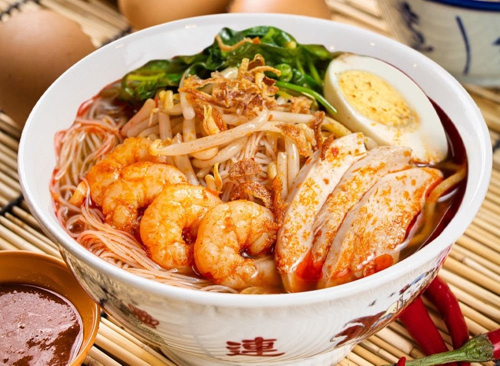 A vibrant bowl of noodles featuring prawns, chicken, egg, and fresh vegetables.