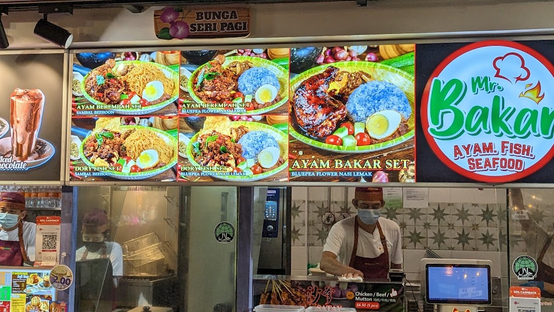A food stall counter with digital menu displays showcasing grilled dishes and staff.