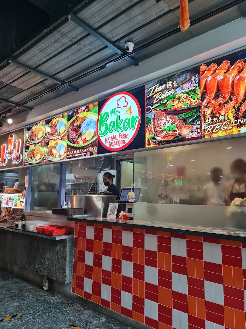 A vibrant food stall counter featuring large display boards showcasing grilled ayam, fish, and seafood dishes.