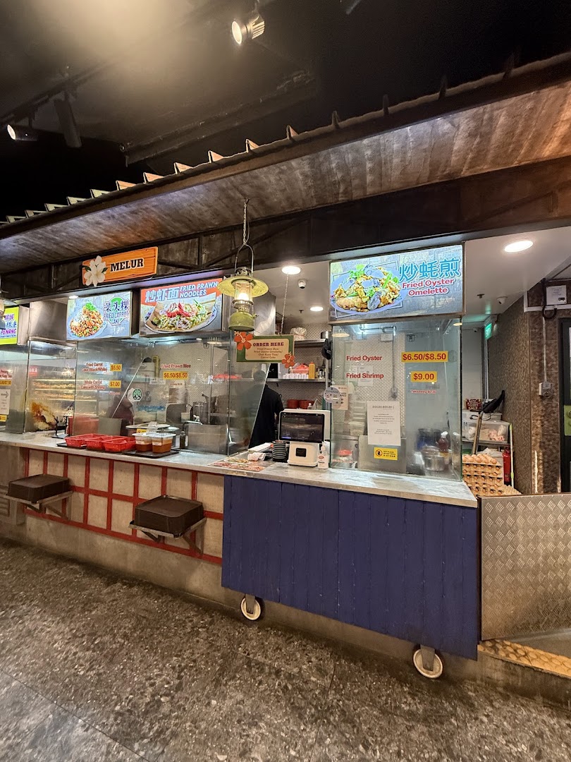 A vibrant food stall counter showcasing various local fried noodle and omelette dishes with prices.