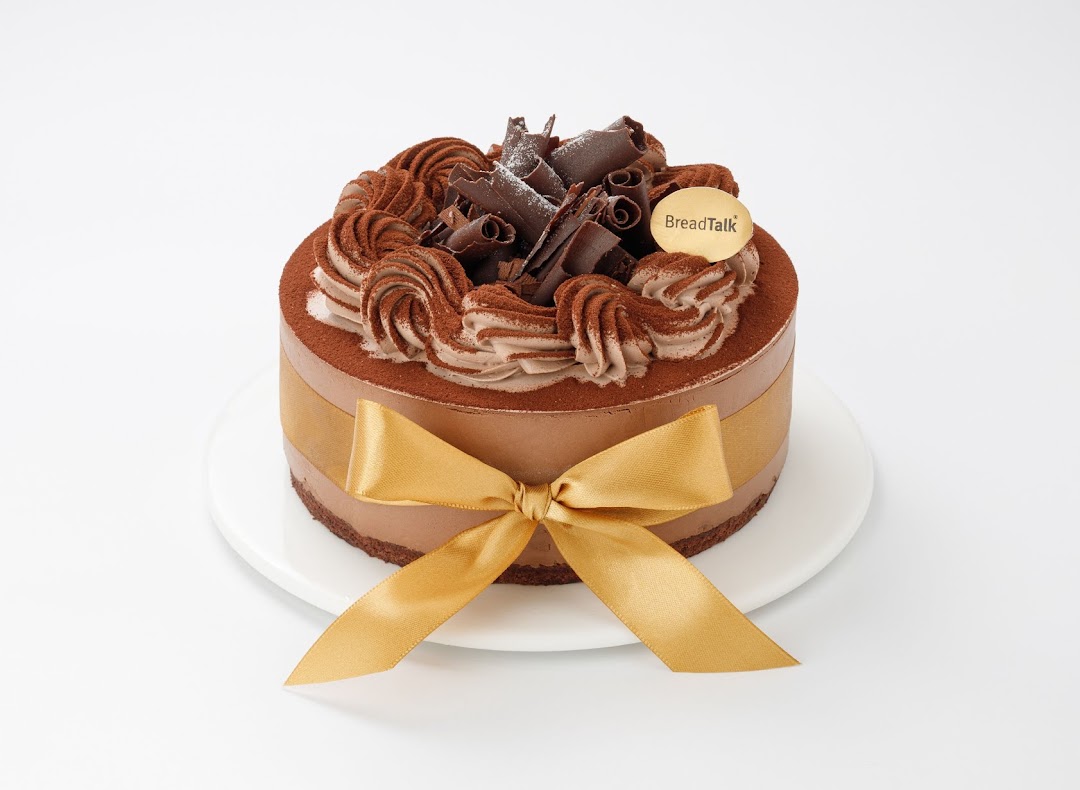 A decadent chocolate cake from BreadTalk, adorned with chocolate curls, cream, and a golden ribbon.
