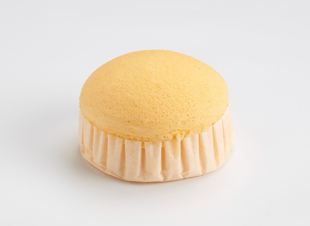 A light, fluffy golden sponge cake in a paper liner on a clean white background.