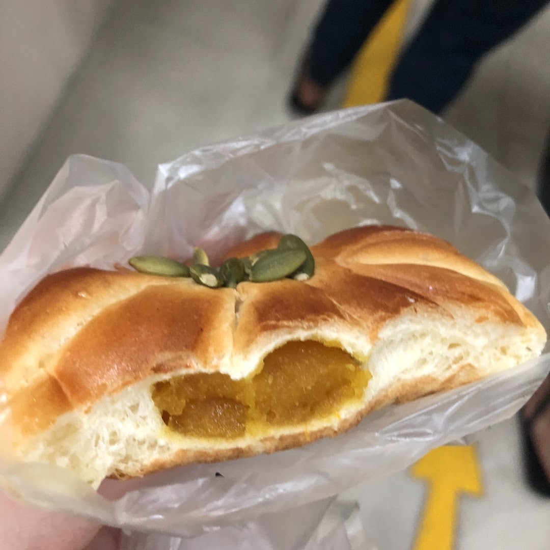 A close-up of a pumpkin-shaped bread with pumpkin filling and pumpkin seeds, held in a plastic bag.