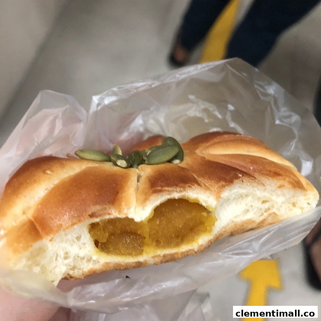 A close-up of a pumpkin-shaped bread with pumpkin filling and pumpkin seeds, held in a plastic bag.