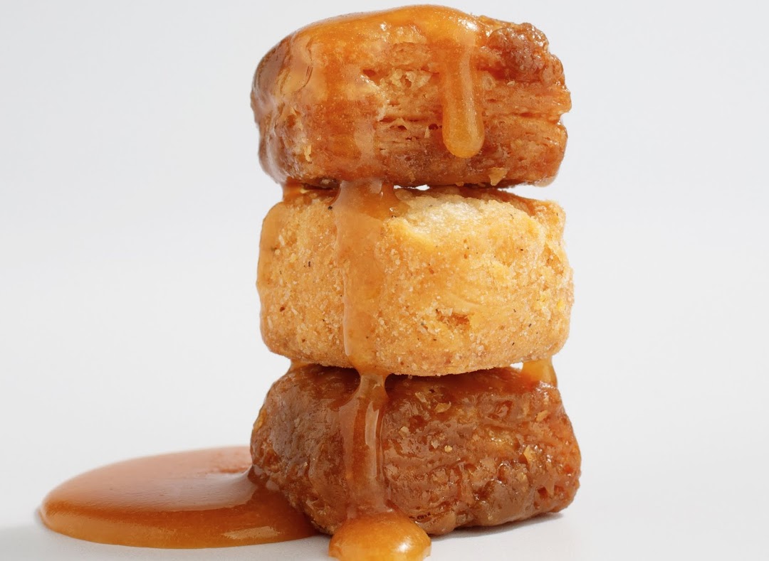 Three golden-brown pastries stacked and generously drizzled with a rich caramel glaze.