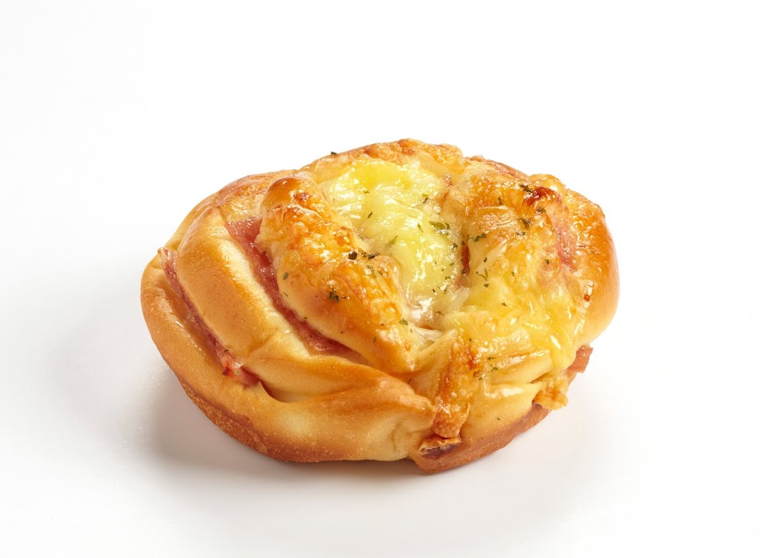 A golden-baked bun topped with melted cheese and herbs, featuring visible ham or bacon filling.