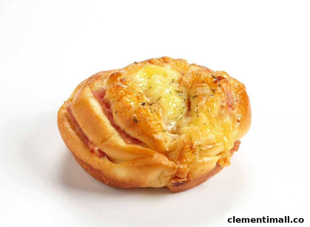 A golden-baked bun topped with melted cheese and herbs, featuring visible ham or bacon filling.