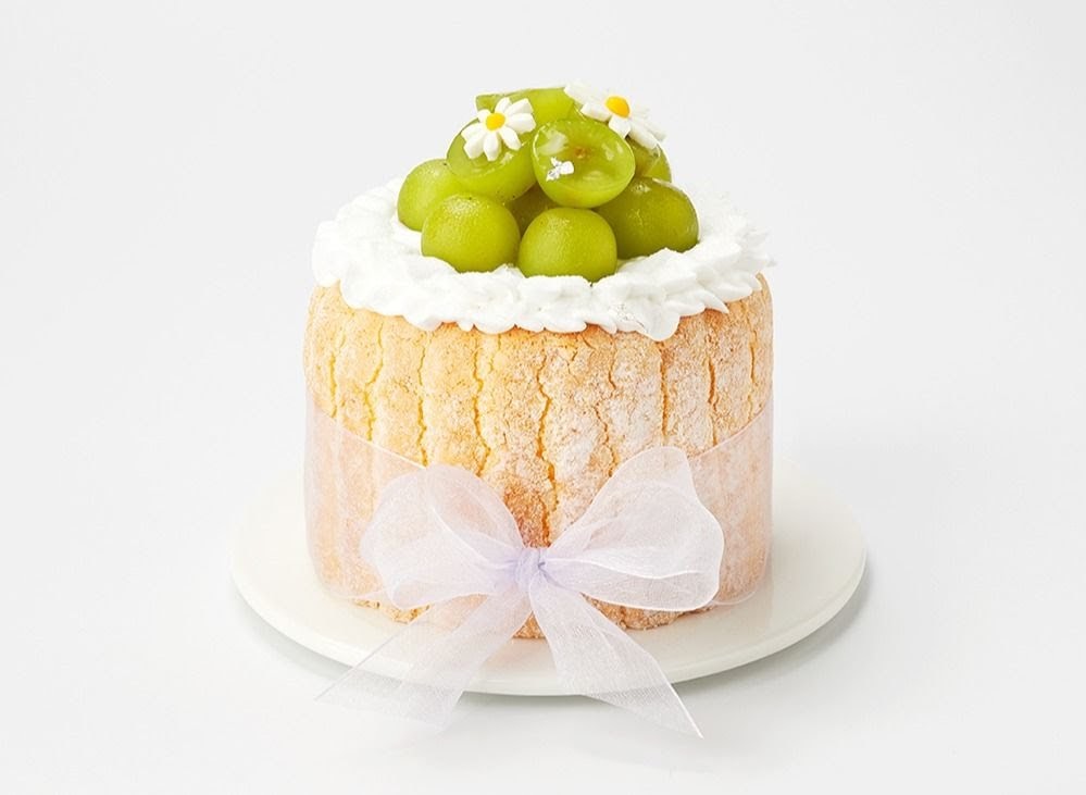 A delightful cake featuring green grapes, whipped cream, and small white flowers, wrapped with a sheer ribbon.