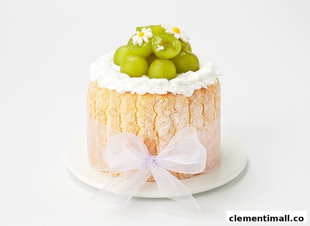 A delightful cake featuring green grapes, whipped cream, and small white flowers, wrapped with a sheer ribbon.