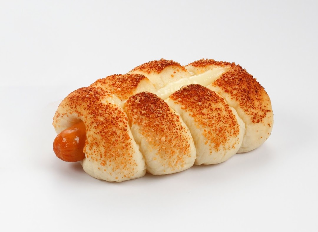 A golden-baked sausage bun with creamy filling and savory breadcrumb topping on a white background.