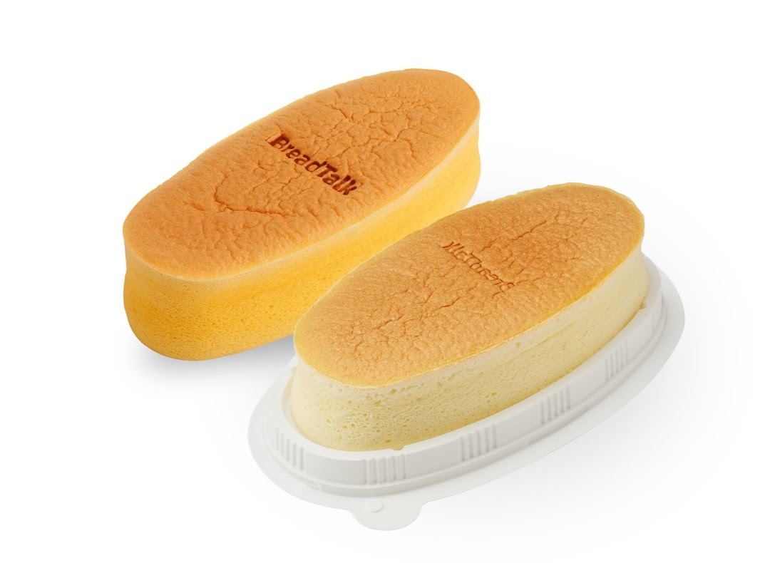 Two golden-brown, oblong sponge cakes, one in a plastic container, on a white background.