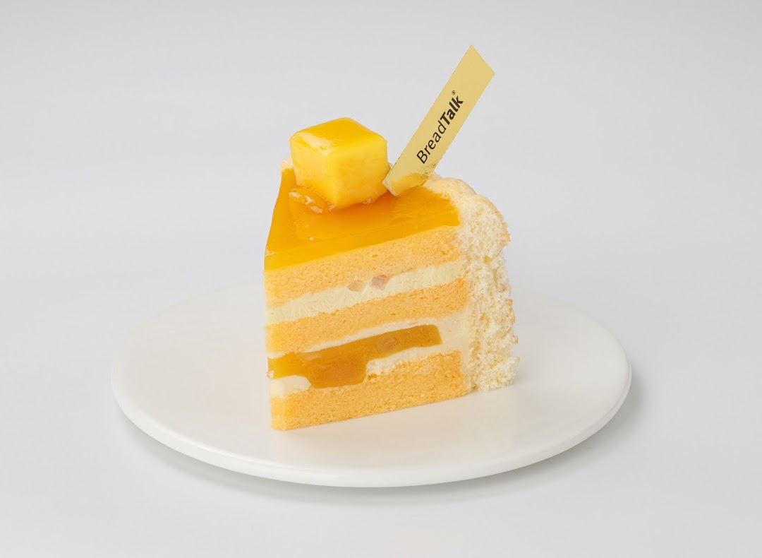 A vibrant slice of mango cake with cream layers and a BreadTalk tag on a white plate.