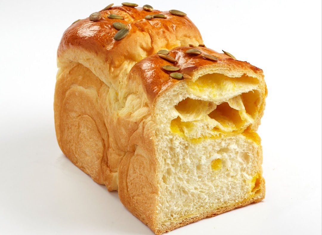 A golden-brown loaf of bread, topped with pumpkin seeds, revealing a soft, yellow interior.