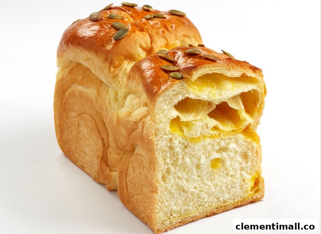 A golden-brown loaf of bread, topped with pumpkin seeds, revealing a soft, yellow interior.