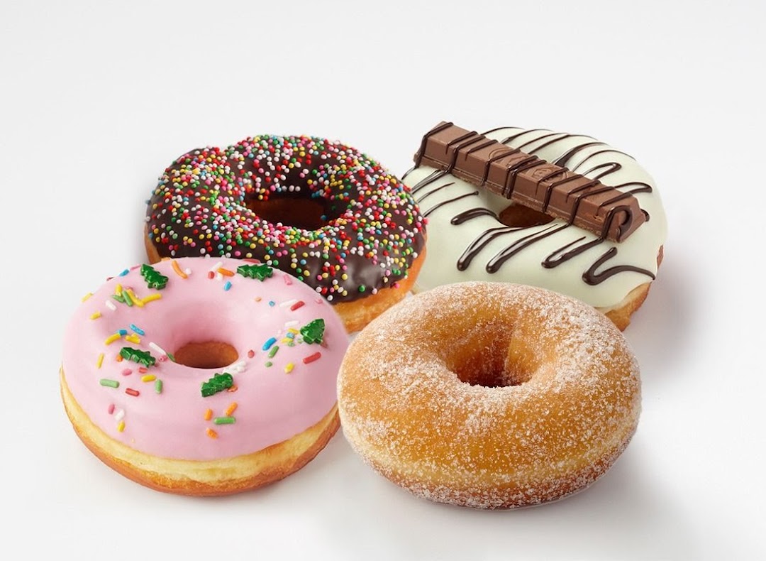 Four colorful donuts with various toppings, including sprinkles, pink icing, sugar, and a chocolate bar.