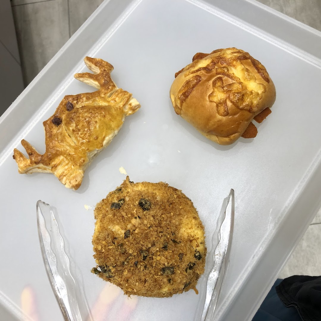 Three distinct baked goods, including a floss bun and a sausage bun, on a white tray with tongs.