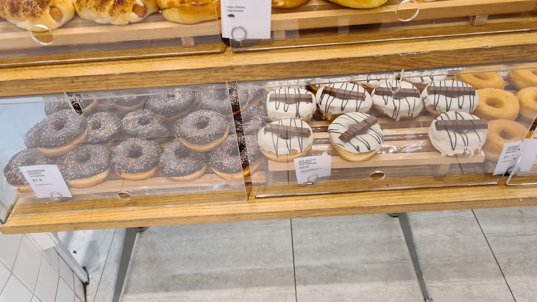 A display case filled with various freshly baked donuts, including chocolate sprinkle and Kit Kat varieties.
