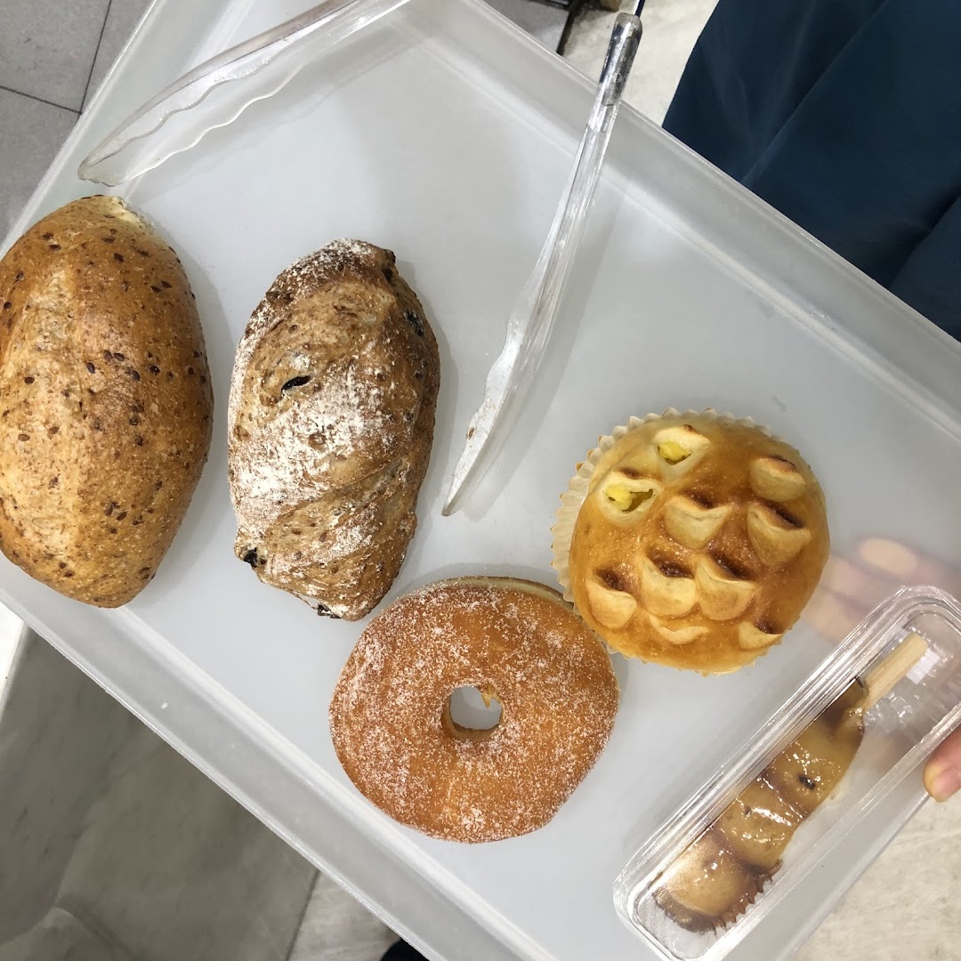 A selection of freshly baked breads, pastries, and a donut on a white tray with tongs.