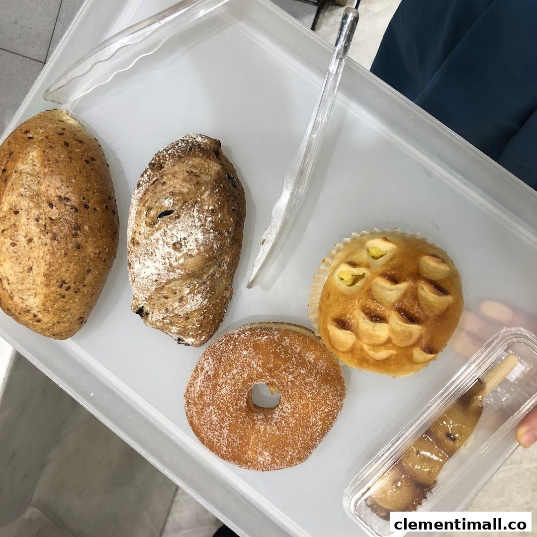 A selection of freshly baked breads, pastries, and a donut on a white tray with tongs.