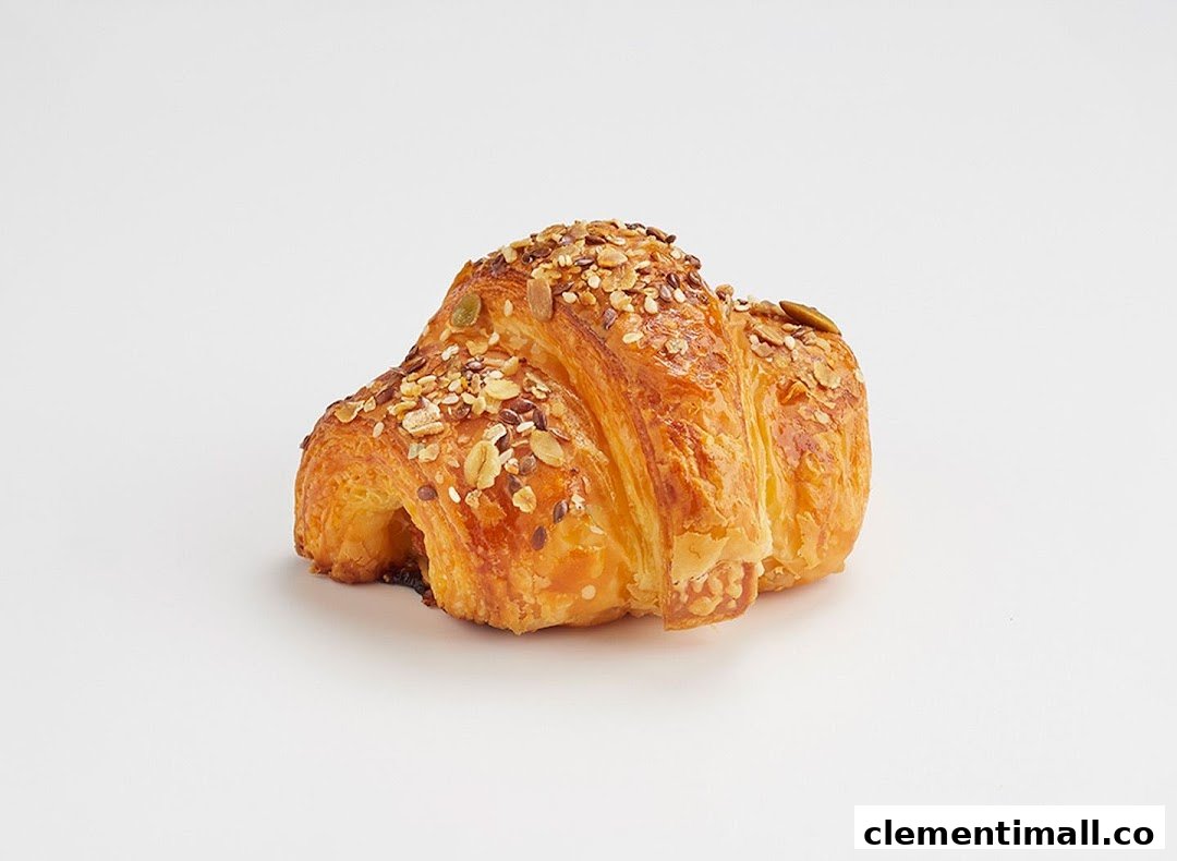 A golden-brown, flaky croissant generously topped with various seeds, presented on a clean white background.