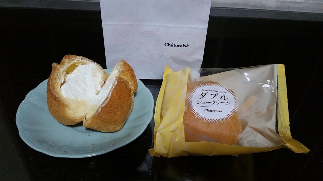 Two Châteraisé cream puffs, one opened on a plate, alongside a branded paper bag.