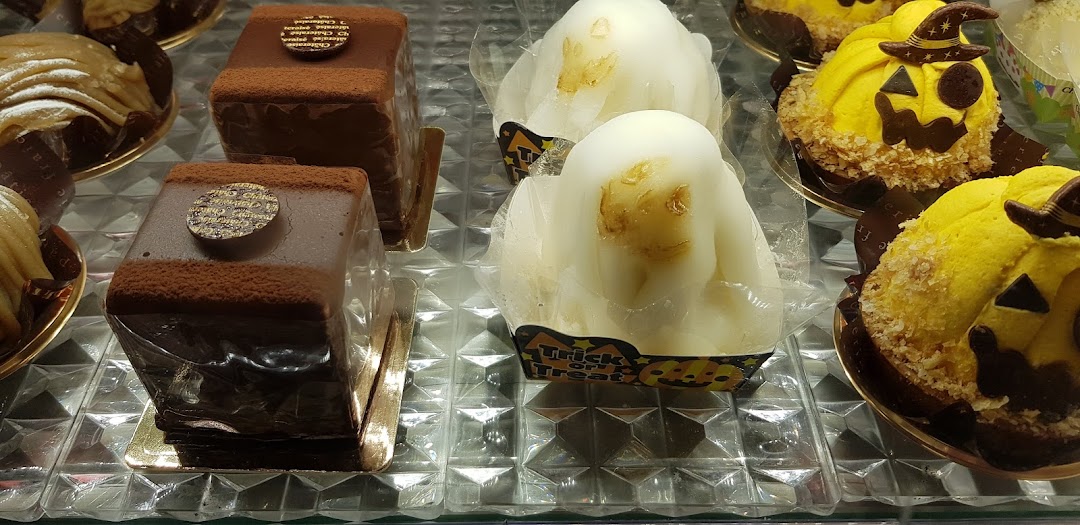 A display case showcasing various cakes, including chocolate pastries and Halloween-themed pumpkin and ghost desserts.