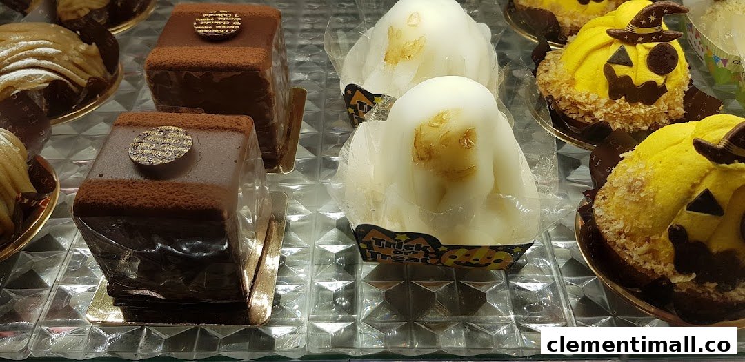 A display case showcasing various cakes, including chocolate pastries and Halloween-themed pumpkin and ghost desserts.