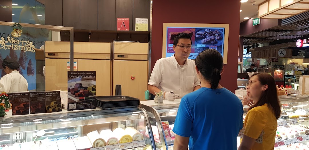 Châteraisé staff assist customers at a vibrant dessert counter displaying cakes, rolls, and chocolates.