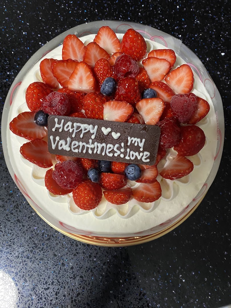 A delicious cream cake topped with fresh strawberries, raspberries, blueberries, and a chocolate Valentine's message.