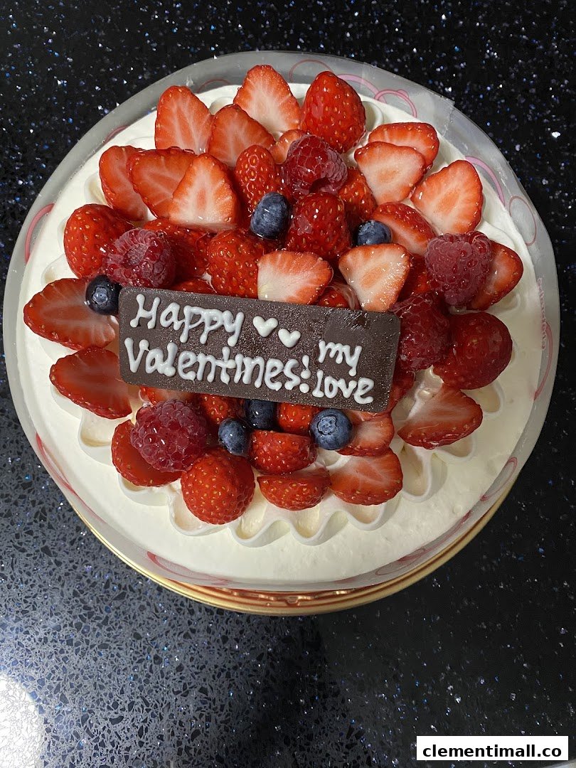 A delicious cream cake topped with fresh strawberries, raspberries, blueberries, and a chocolate Valentine's message.