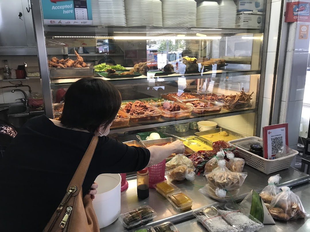 A customer selects dishes from a vibrant display of local food at a bustling eatery counter.