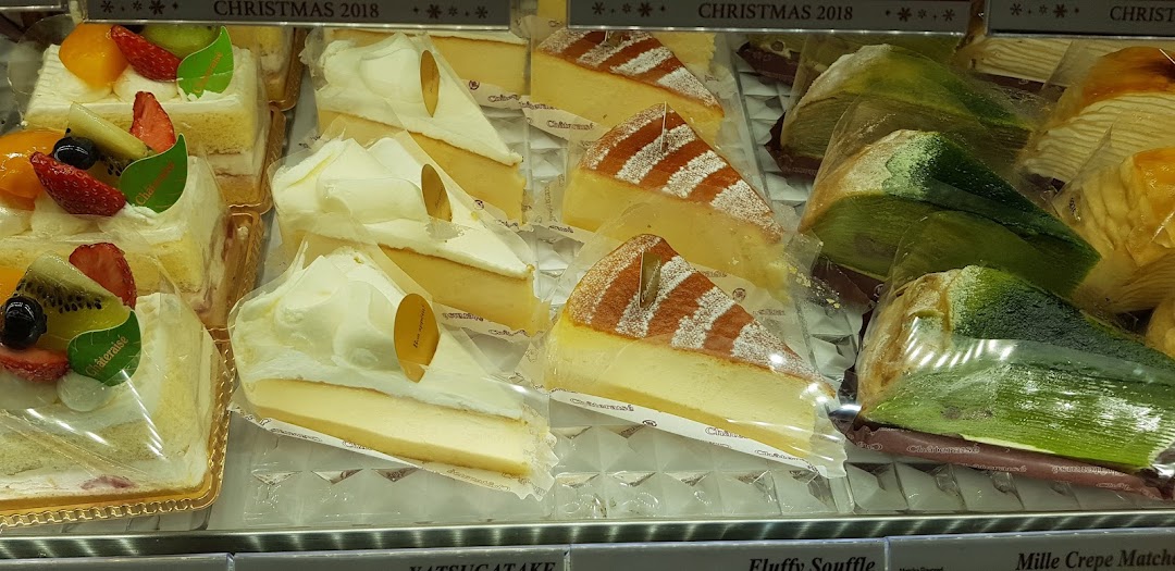 A vibrant display of various cakes, including fruit tarts, cheesecakes, and matcha crepes, in a retail display.